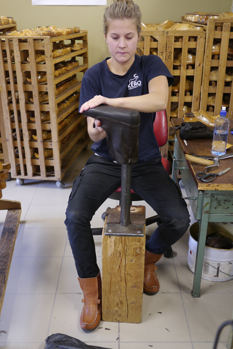 Kvinna sitter och jobbar på en lädersko i verkstad.