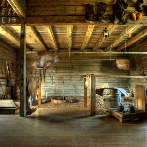 Bild innifrån gamla garveriet på Keros. Bilden visar en gedigen träbyggnad med diverse läderföremål som hänger i tak och väggar.
