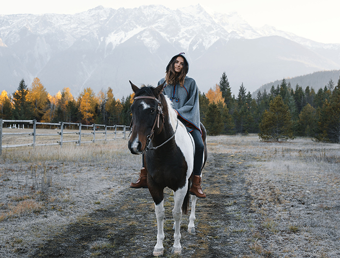 Anna Lengstrand sitter med huvtröja på en brun och vit häst utomhus