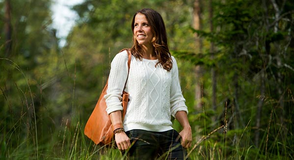 Charlotte Kalla står i skogen och tittar åt vänster, hon är iförd vit tröja och läderväska från Kero.